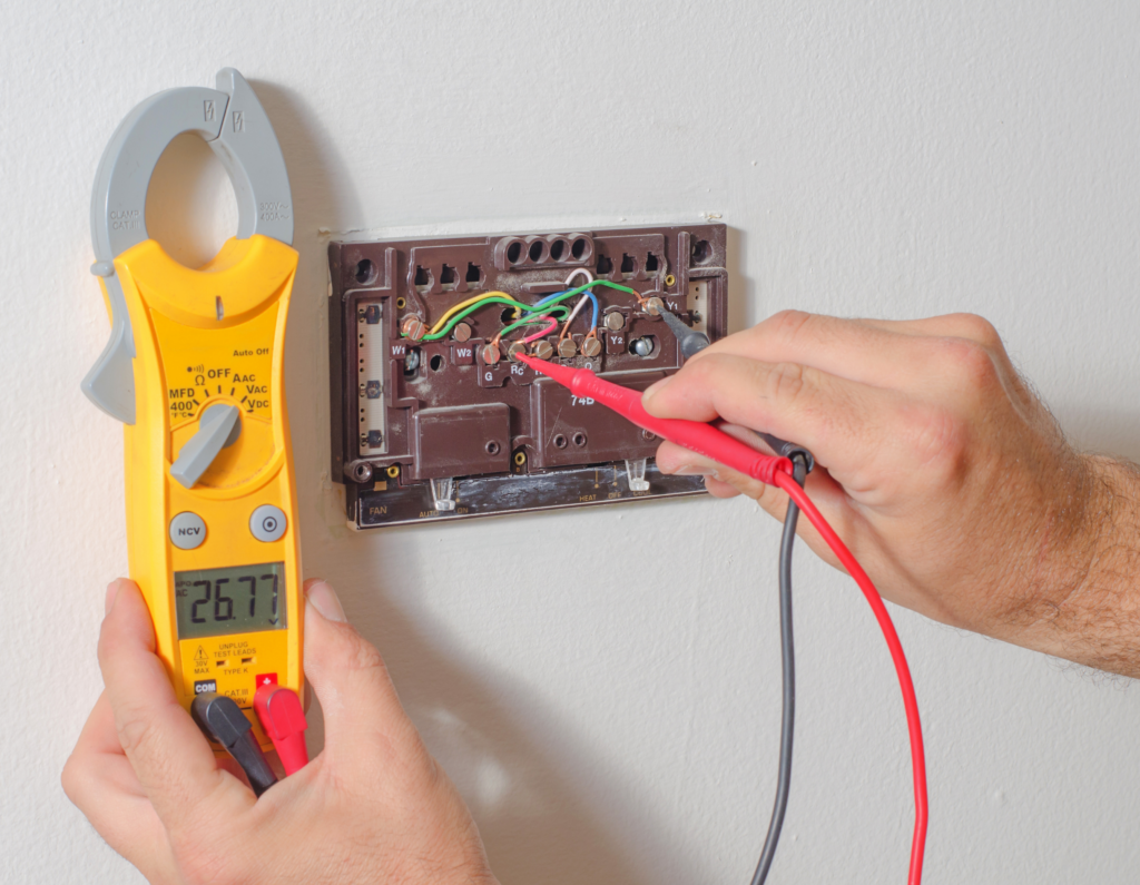 echnician performing thermostat repair using a multimeter to test wiring connections.